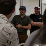 A photo of a man with a green shirt and hat standing at a gathering.