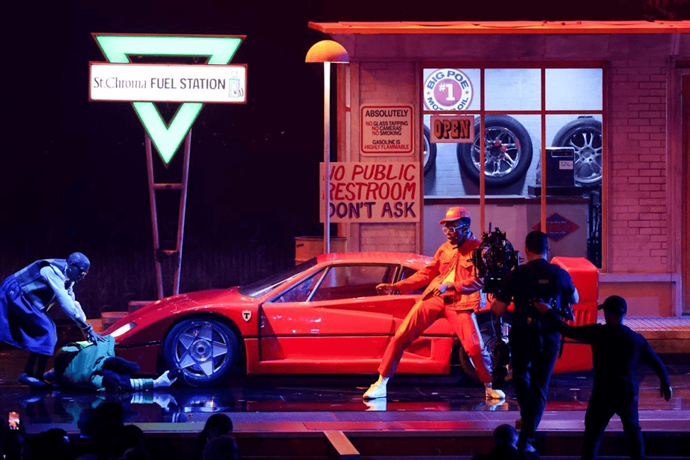 Tyler The Creator performing at the Grammys in front of a red car and gas station set.